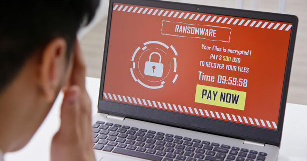 Mann ser frustrert på en laptop-skjerm hvor det har kommet opp en melding om "ransomware" og "pay now".